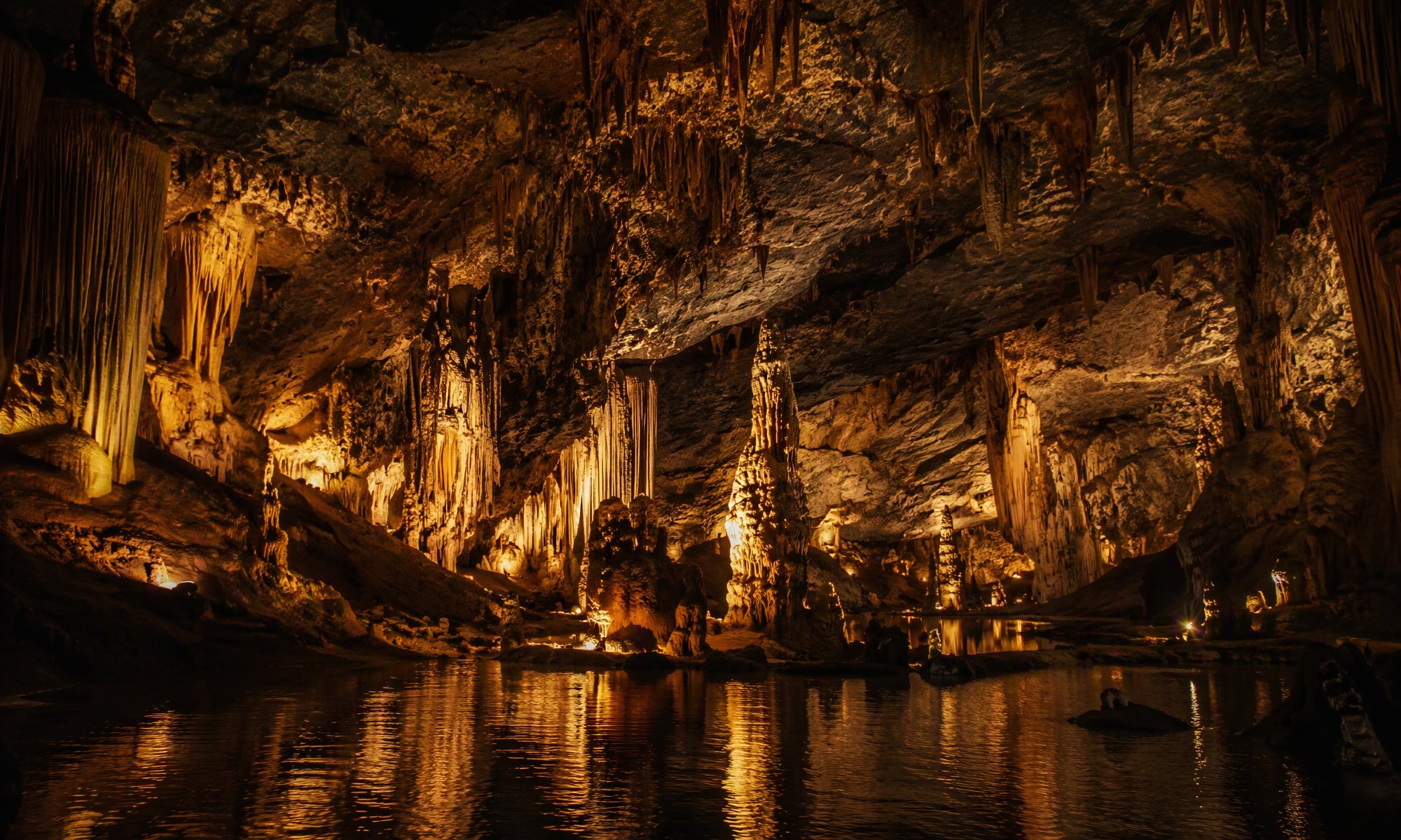 Vast underground cave hall with dripstone formations and a reflective pool
